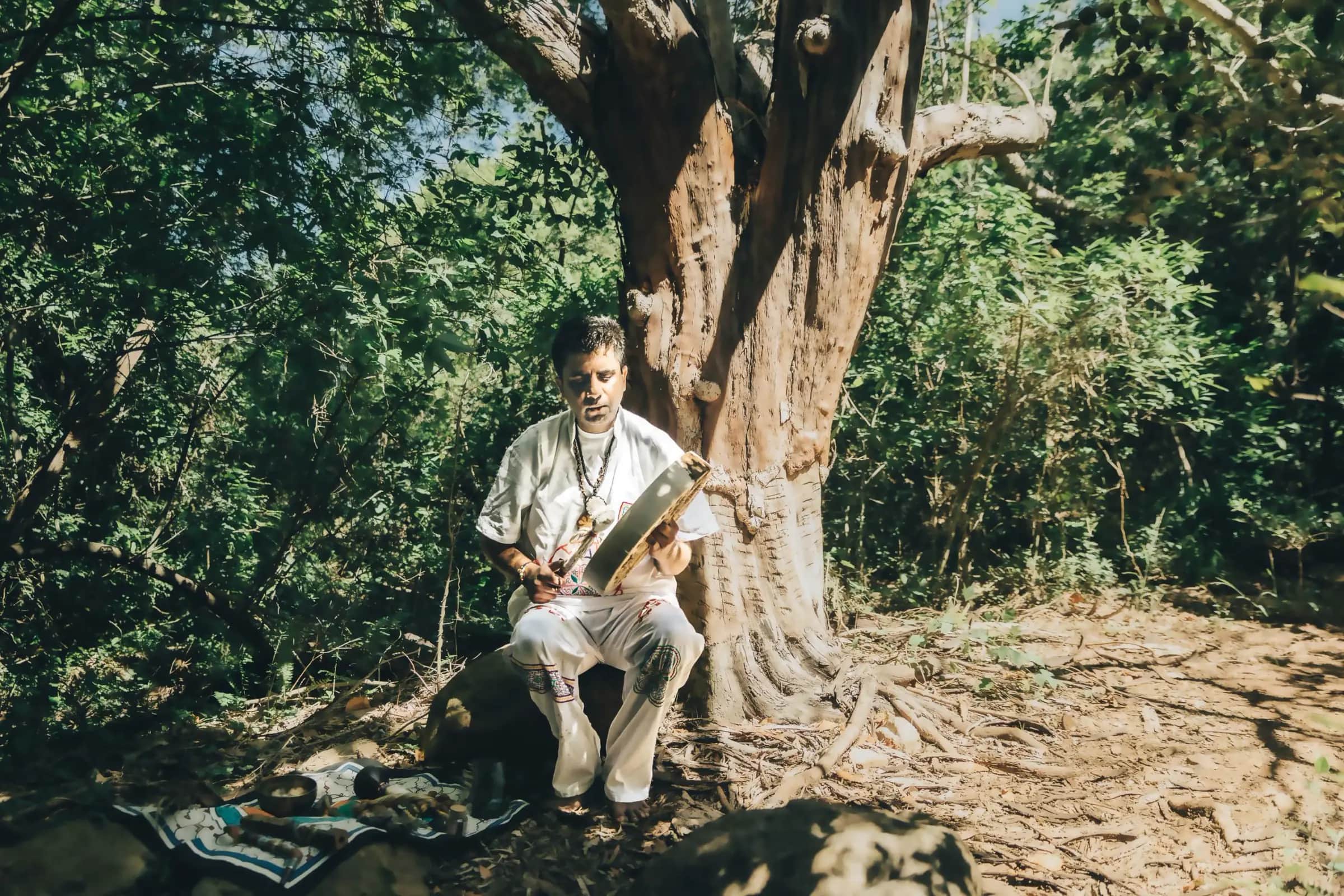 Jayesh Mitha (MINJAY) playing a frame drum beneath a tree — Ayahuasca and plant medicine ceremonies in Cape Town